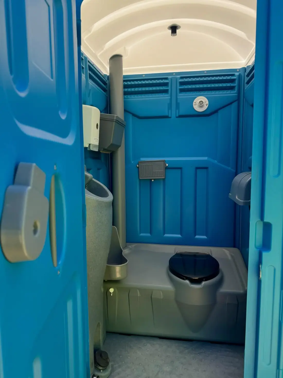 Inside a blue standard porta potty showing the urinal, seat and paper holder